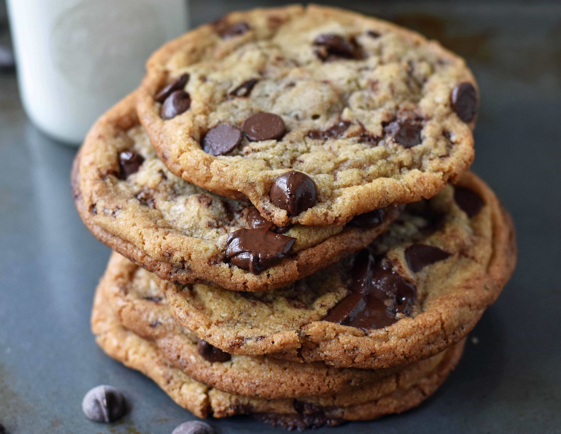 A stack of gooey chocolate chip cookies beside a jar of milk